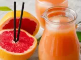 Orzeźwiający sok z grejpfruta w dzbanku i szklance, obok przekrojonych owoców. Idealny na upalne dni.