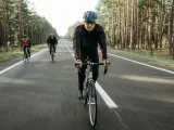 Cyclists on a road through a forest, likely engaged in a VO2 max training program, pushing their limits.
