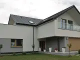 Nowoczesna elewacja budynku z szarymi i białymi tynkami, dużym oknem, balkonem i drewnianą bramą garażową.