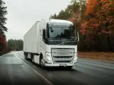 Biała ciężarówka Volvo FH12 z naczepą jedzie po mokrej drodze wśród jesiennego lasu.