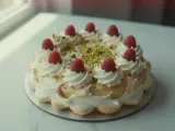 Wykwintny tort pistacjowo malinowy, ozdobiony bitą śmietaną, malinami i posypką z pistacji.