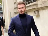 David Beckham luce un elegante traje azul con jersey de cuello alto, caminando con confianza.