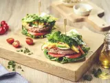 Dwa soczyste burgery w sałacie, z pomidorami, ogórkiem i papryką, na drewnianej desce.