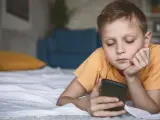 Chłopiec leży na łóżku, patrząc na telefon. Zastanawia się, co to jest sexting i jakie niesie zagrożenia.