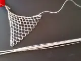 Un ago con filo bianco e un pezzo di rete a maglie, un tipo di ricamo eseguito su una rete a maglie, con un nastro rosso in alto.