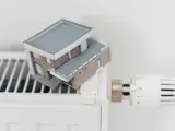 Model domu na grzejniku symbolizuje wysokie koszty ogrzewania i potrzebę dopłat do prądu.
