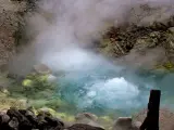 Gorący, bulgoczący onsen otoczony skalistym, parującym krajobrazem. Woda ma turkusowy odcień, a brzegi pokryte są żółtymi osadami.