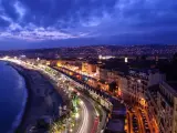 Night view of the Promenade des Anglais from Castle Hill, Nice, France, with city lights twinkling and car trails on the road.