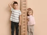 Chłopiec i dziewczynka mierzą wzrost przy drewnianej miarce. Chłopiec ma ok. 120 cm, dziewczynka ok. 80 cm.