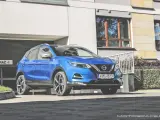 Błękitny Nissan Qashqai 2018 zaparkowany przed nowoczesnym budynkiem z garażem.