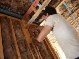 Pracownik montuje wełnę mineralną w konstrukcji dachu. Utylizacja wełny mineralnej to ważny etap budowy.