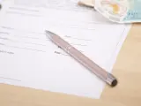 Długopis na dokumencie z polami do podpisu i daty. Obok leżą banknoty. To może być beesafe wypowiedzenie oc.