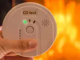 Detektor czadu z zieloną diodą i napisem "CO test" na tle płomieni.