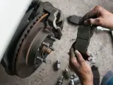 Mechanik pokazuje zużyte klocki hamulcowe przed ich wymianą. Sprawdź wymiana klocków hamulcowych cena.