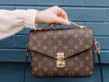 Una mano tiene una borsa Louis Vuitton con il classico monogramma. Un'icona di stile, che ci ricorda dove louis vuitton nasce: dalla maestria artigianale francese.