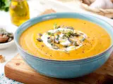 Vellutata di zucca cremosa, guarnita con panna, semi di zucca e timo, servita in una ciotola azzurra su un tagliere di legno.