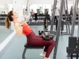 Kvinna tränar rakarmade latsdrag på gym.