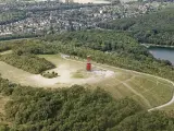 Luftaufnahme der Halde Rheinpreußen mit rotem Geleucht, umgeben von Wald und einem See.