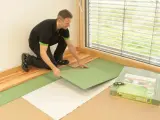 Mężczyzna układa zieloną matę, która stanowi podkład pod panele i ogrzewanie podłogowe. Obok leży opakowanie z materiałem.