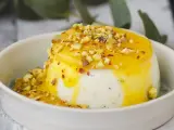 Budino fatto in casa cremoso, con salsa gialla e granella di pistacchi, servito in una ciotola bianca.