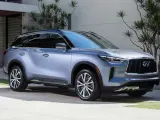 Elegancki, srebrny Infiniti SUV zaparkowany przed nowoczesnym domem z bujną roślinnością.