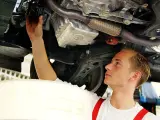 Ein junger Mechaniker bei einer Arbeitsstunde in der Kfz Werkstatt wechselt den Ölfilter unter einem Auto.