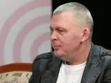 Adam z zespołu Raz Dwa Trzy w szarej marynarce, siedzi na kanapie.
