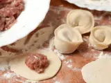 Przygotowanie pierogów z mięsem mielonym surowym. Na drewnianej desce widać surowe ciasto, farsz i gotowe pierożki.