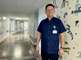Mężczyzna w granatowym uniformie medycznym stoi na tle szpitalnego korytarza z kolorowymi grafikami.