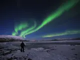 En ensam person står på en isig strand och ser på det magiska abisko norrsken som dansar över himlen.