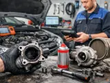 Mechanik trzyma mocno zabrudzony zawór EGR. Obok leżą turbosprężarka i narzędzia.