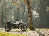 Biały motocykl z sakwami, zaparkowany przy drzewie w lesie. Idealny do testów w rankingu opon motocyklowych.