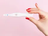Dłoń z czerwonymi paznokciami trzyma test ciążowy z dwoma kreskami. To może być sygnał, że doszło do ciąży biochemicznej.