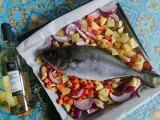 Ricciola al forno pronta per essere infornata con patate, carote e cipolle rosse. Accanto, una bottiglia di vino bianco.