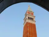 Vista dal campanile di San Marco: la torre in mattoni rossi si staglia contro il cielo azzurro, incorniciata da un arco di pietra.