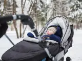 Śpiące dziecko w wózku zimą. Ciepły kombinezon, czapka i rękawiczki to podstawa, co włożyć do wózka dla noworodka zimą.