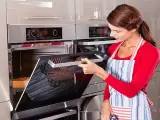 Mujer con delantal abre horno donde se hornea un pan.
