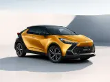 Nowy, złoty Toyota C-HR Hybrid z czarnym dachem prezentuje się dynamicznie na tle minimalistycznej architektury.