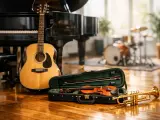 Eine wunderschöne erste Gitarre steht neben einem Flügel. Ein Geigenkasten mit Geige und Bogen sowie eine Trompete liegen auf dem Holzboden.