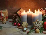Vier brennende Kerzen im **Hintergrund Adventszeit**, umgeben von Tannenzweigen, Geschenken, Nüssen und Weihnachtsplätzchen.