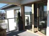 Nowoczesny balkon z drewnianymi, podwójnymi drzwiami balkonowymi. Okna dzielone poziomo wpuszczają dużo światła.