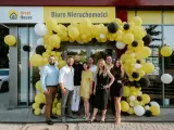 Grupa ludzi pozuje przed biurem nieruchomości ozdobionym żółtymi balonami.