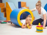 Dla kogo wczesne wspomaganie rozwoju? Dla małej dziewczynki bawiącej się w tunelu z terapeutką.