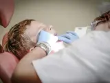 Chłopiec siedzi na fotelu dentystycznym podczas wizyty u dentysty. Dentysta w rękawiczkach bada jego zęby.