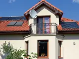 Elegancki wykusz w domu z balkonem i anteną satelitarną. Na dachu widoczne kolektory słoneczne.