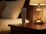 En tub med hudvårdsprodukt står på ett nattduksbord bredvid en säng. Produkten är framtagen för olika hudtyper.