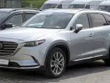 Srebrna Mazda CX-9 z napisem "PRE-OWNED" na przedniej szybie, zaparkowana na zewnątrz.