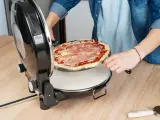 Osoba wkłada surowe ciasto na pizzę z szynką do okrągłego piekarnika.