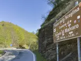 Cartello stradale indica "Passo della Scoglina, Favale di Malvaro, altit. 920 m. s.l.m." su una strada di montagna con vegetazione lussureggiante.