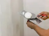 Mani che usano spatole per applicare stucco su un muro. Lo stucco serve a livellare e riparare le imperfezioni.